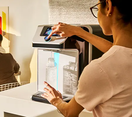 A person filling a reusable bottle at a modern countertop water dispenser.