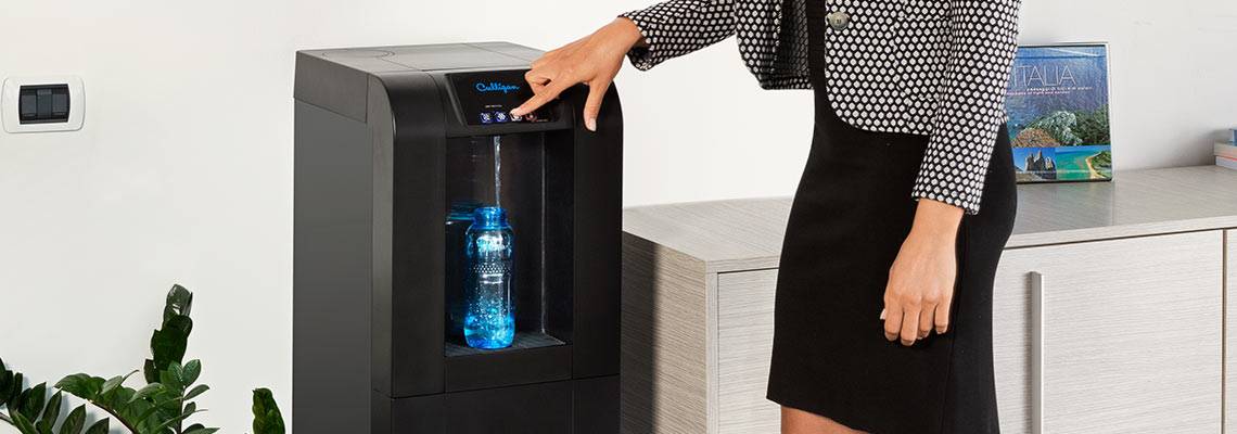 Woman using mains-fed culligan water cooler to fill a bottle with water