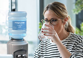Woman in stripy shirt drinking a glass of water with a water cooler in the background