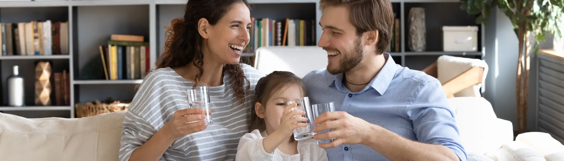 mother, father and daughter sat on sofa drinking water