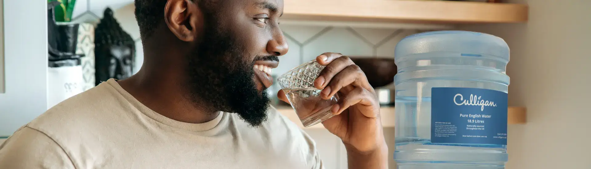 man drinking glass of water with bottled water cooler in background